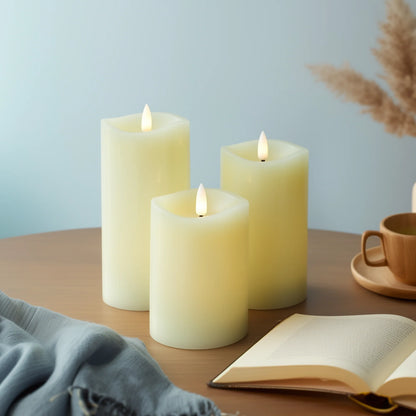 Three lit candles on a table with a book, mug, and dried plants in the background.