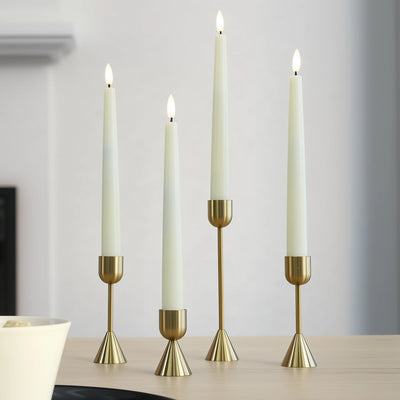 Four tall candles in gold candle holders on a neutral background