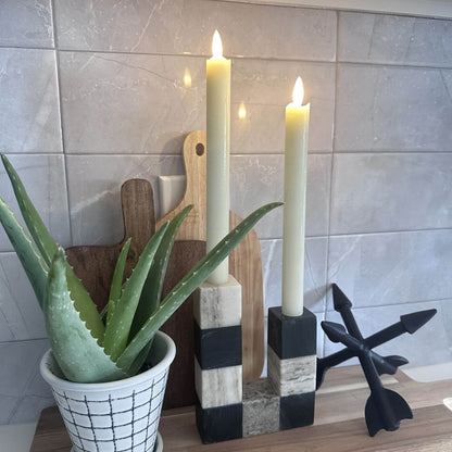 Decorative candles on a stand with a potted aloe vera plant and wooden cutting board against a tiled wall.