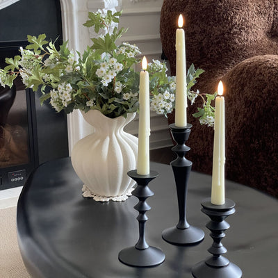Decorative setup with candles in black holders and a vase of flowers on a table.