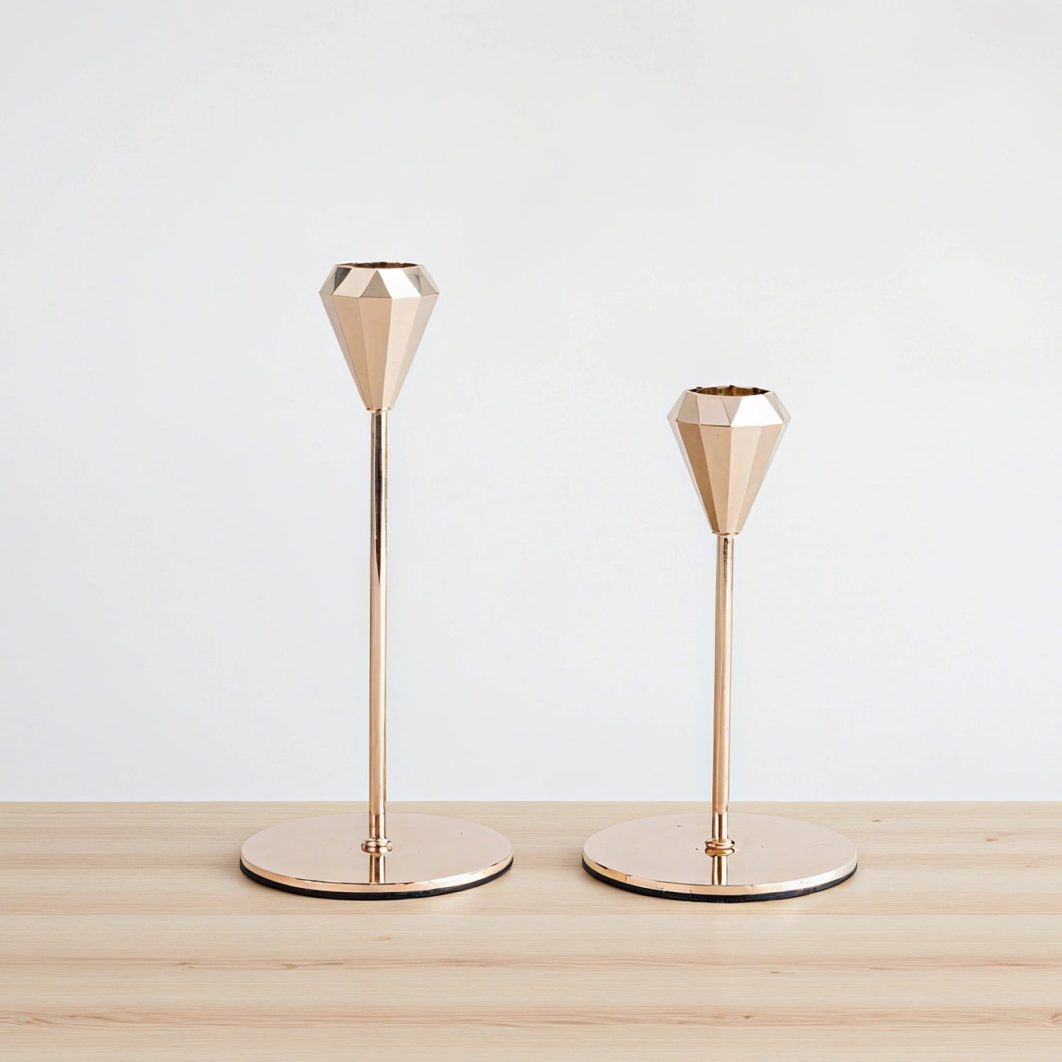 Two gold geometric candle holders on a wooden surface with a white background