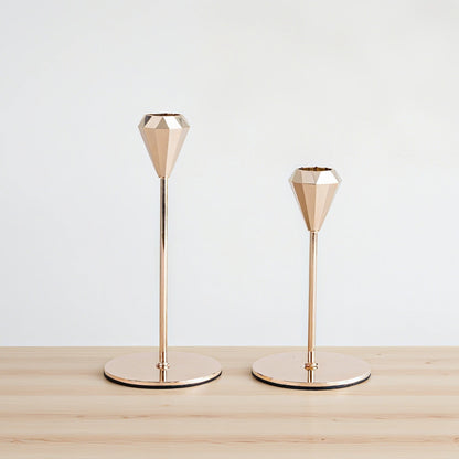 Two gold geometric candle holders on a wooden surface with a white background
