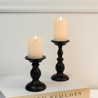 Two candles in black candlesticks on a white surface with a neutral background