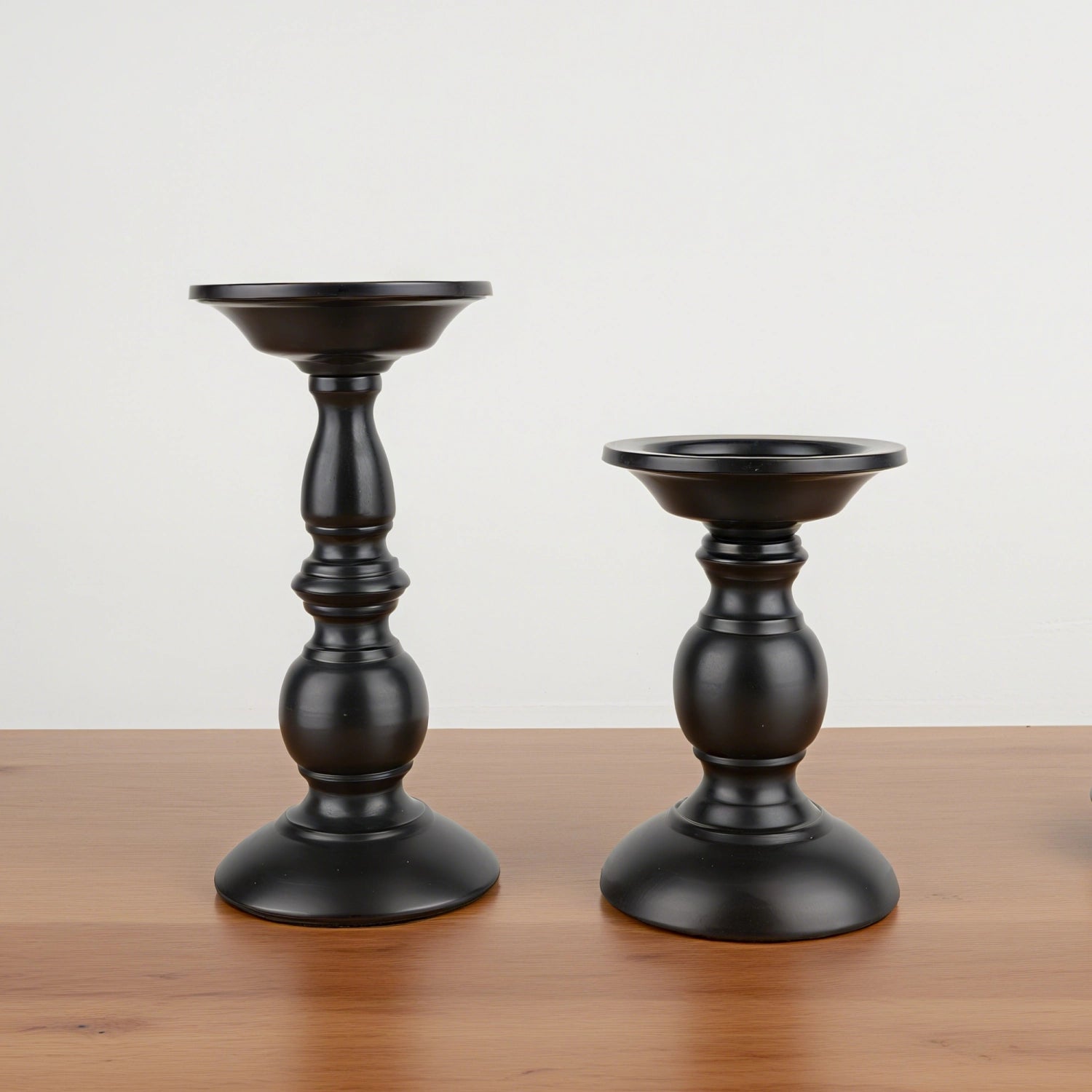Two black candle holders on a wooden surface with a light gray background