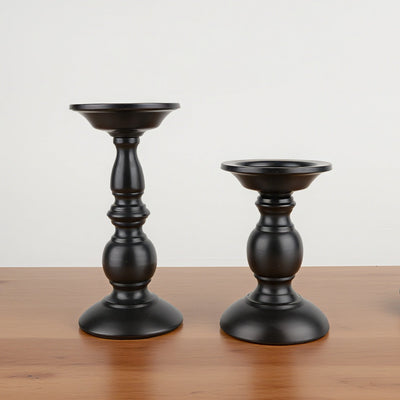 Two black candle holders on a wooden surface with a light gray background