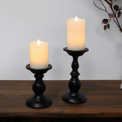 Two black candle holders with lit candles on a wooden surface.