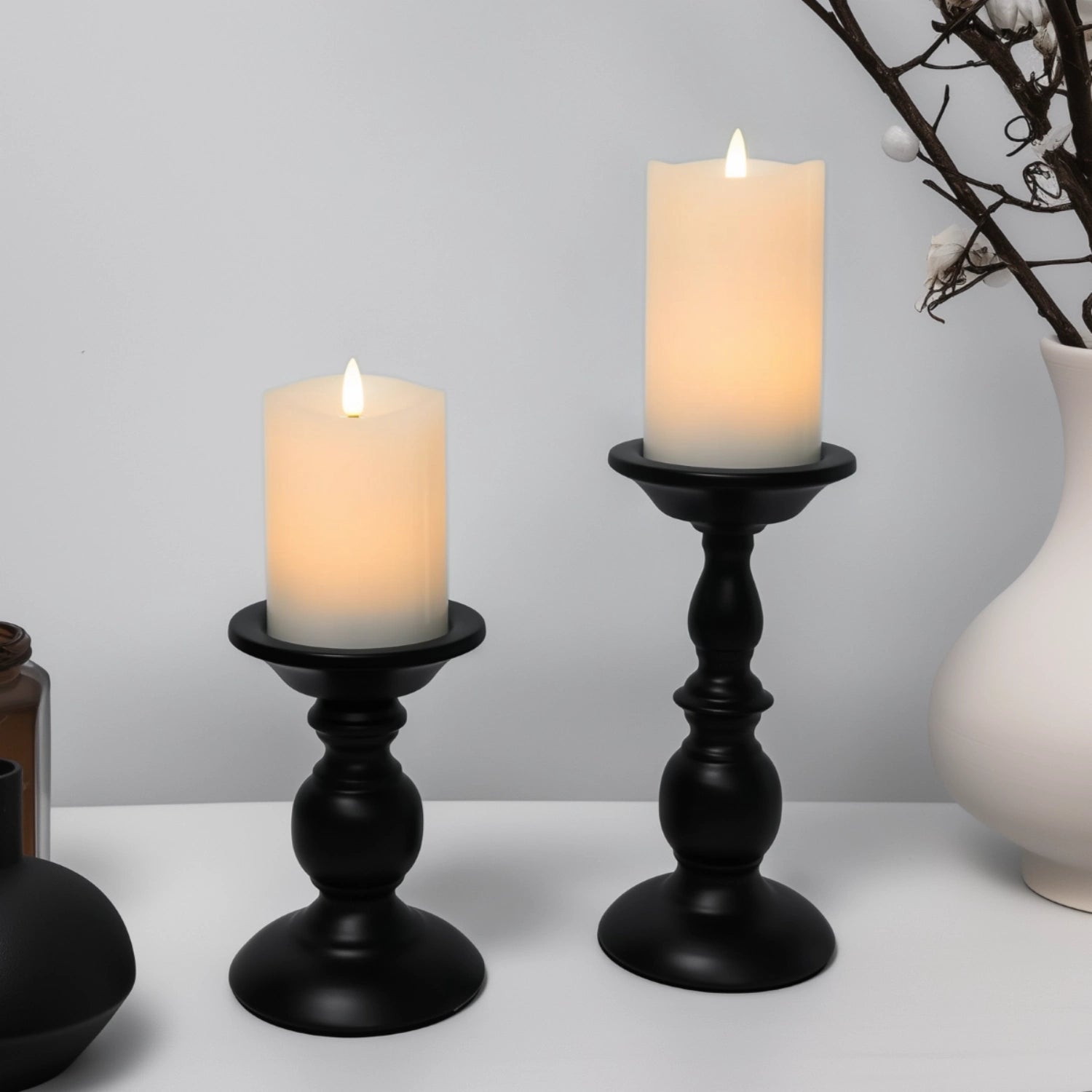 Two lit candles in black candle holders on a white surface with a gray background