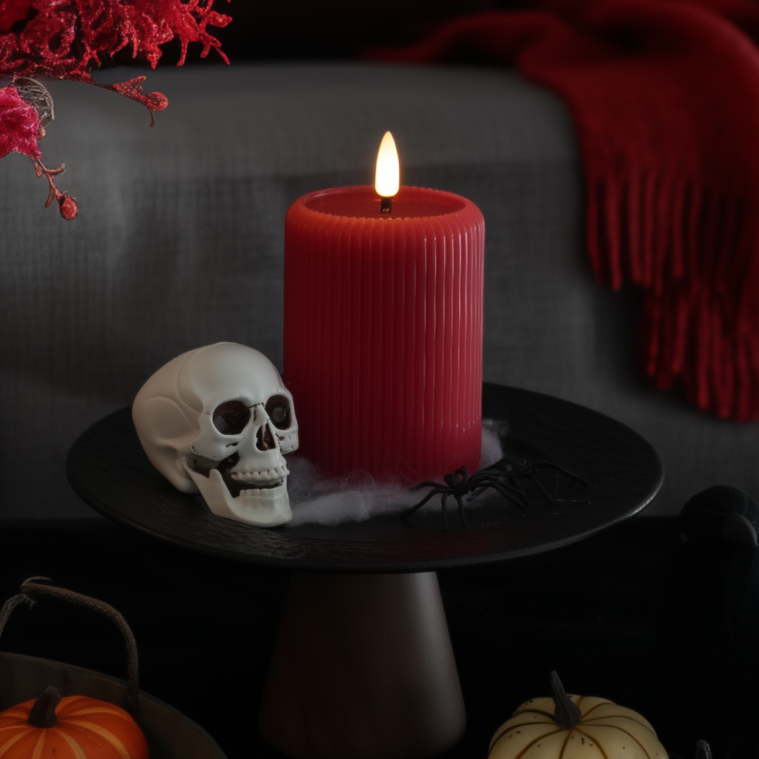 Halloween-themed setting with a red candle, skull, and pumpkins on a dark surface.#color_red