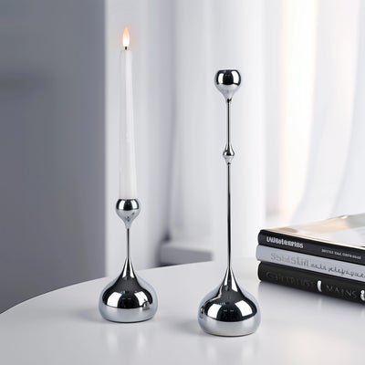 Two silver candle holders on a white surface with a blurred background