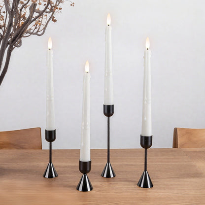 Set of four white candles in black candle holders on a wooden table with a neutral background.