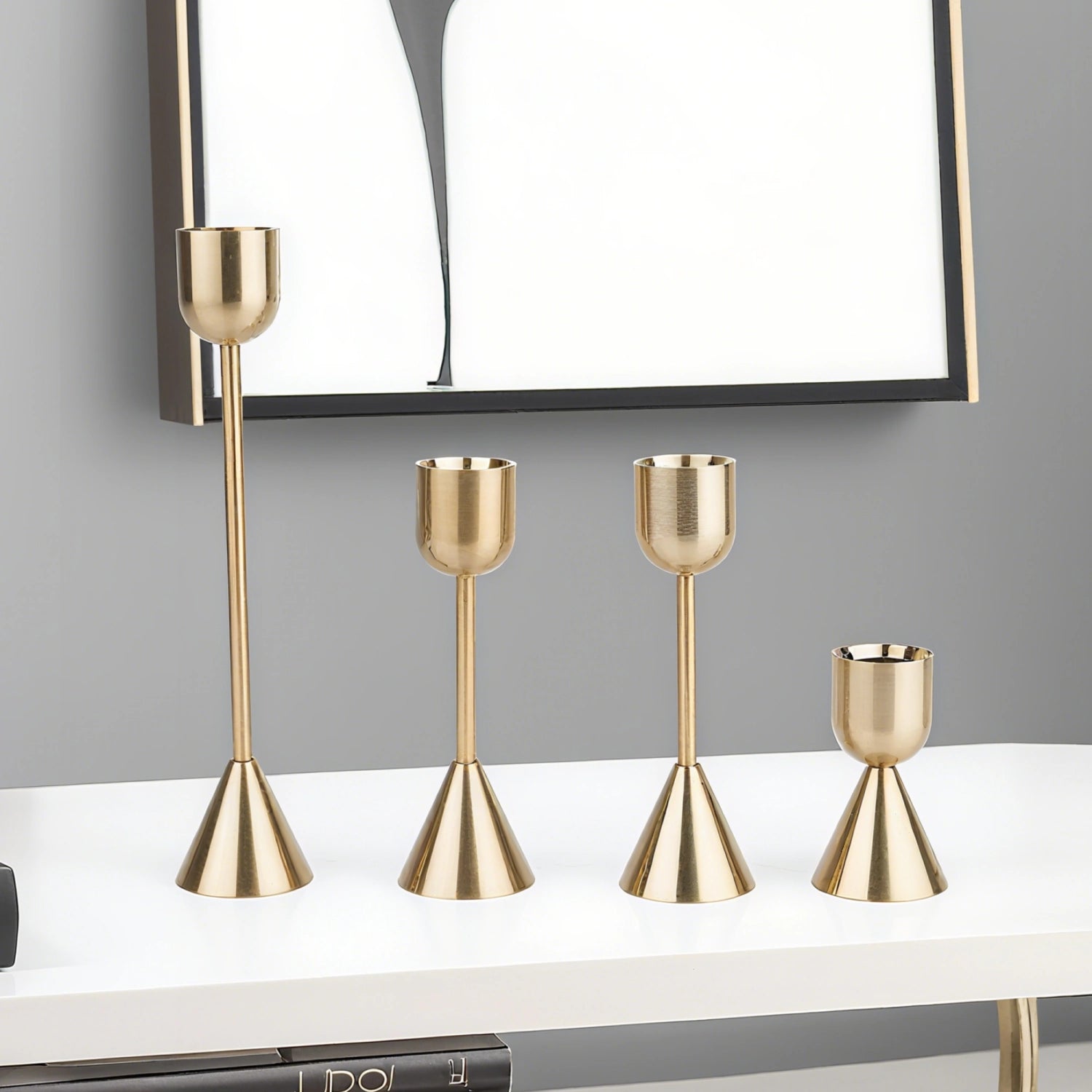 Set of four gold candle holders on a white surface with a gray wall background