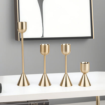 Set of four gold candle holders on a white surface with a gray wall background