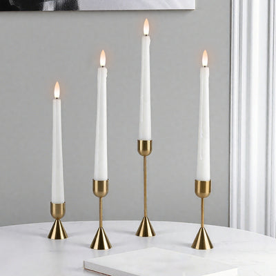 Four white candles in gold candle holders on a white surface with a gray wall background.