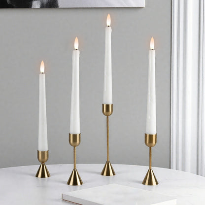 Four white candles in gold candle holders on a white surface with a gray wall background.