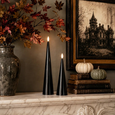 Black cone-shaped candles with lit flames on a table with Halloween decorations.