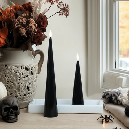 Two black candles on a white tray with decorative elements including a skull and spider in a room setting.