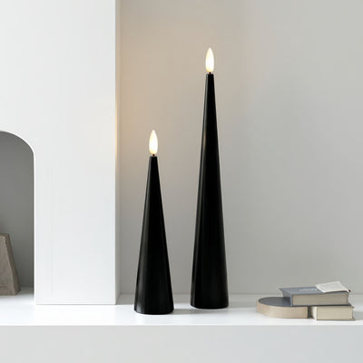 Black cone-shaped candles with lit flames on a table with Halloween decorations.