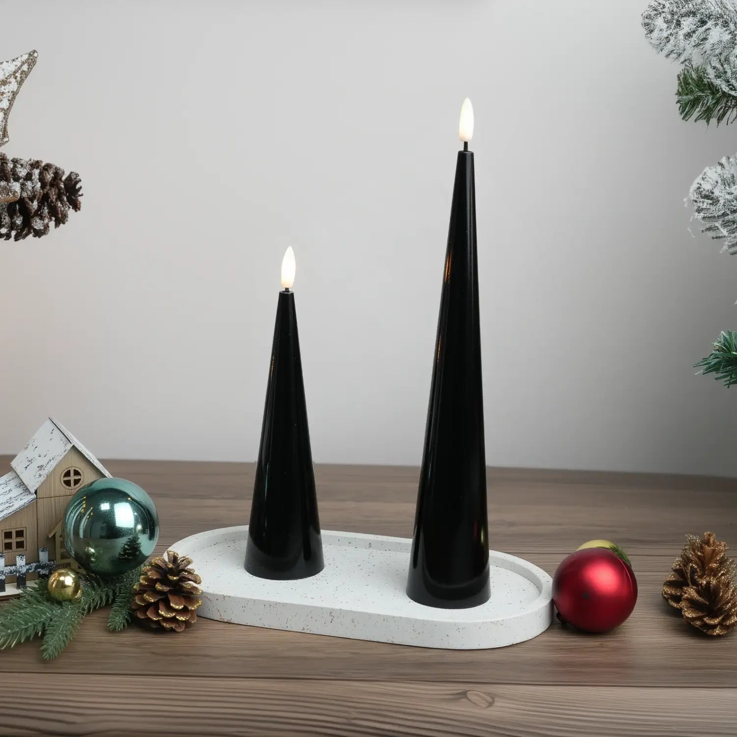 Two black taper candles on a white tray with decorative elements in the background.