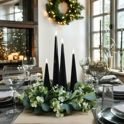 Decorative table setting with black candles and greenery in a home setting.