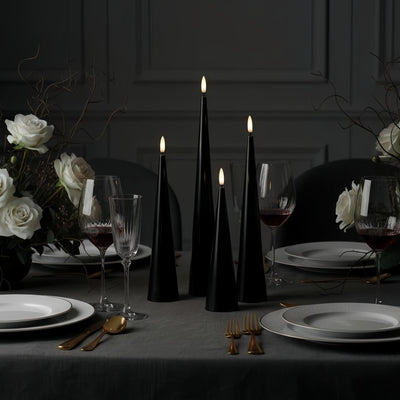 Black candles on a wooden base with a Christmas tree in the background