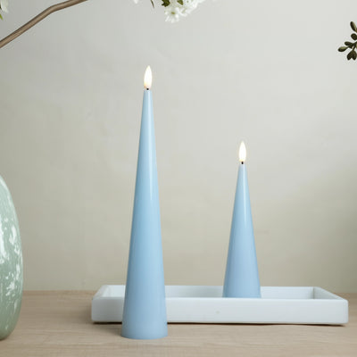 Two light blue cone-shaped candles on a white tray with a neutral background