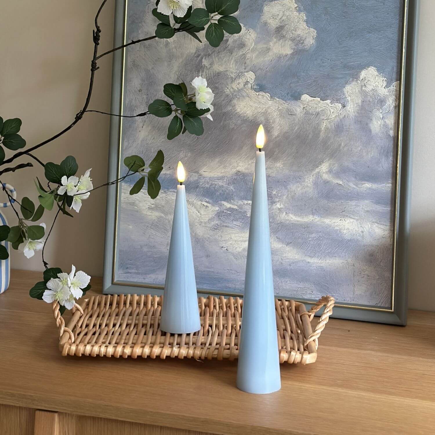 Two light blue cone-shaped candles with a vase of flowers on a wooden surface.