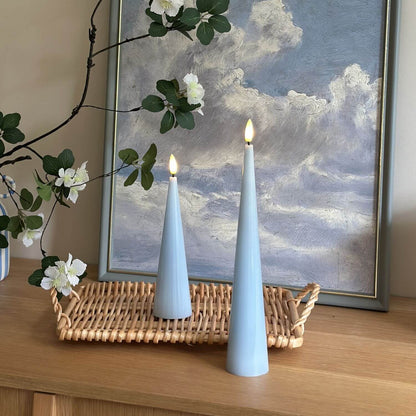 Two light blue cone-shaped candles with a vase of flowers on a wooden surface.