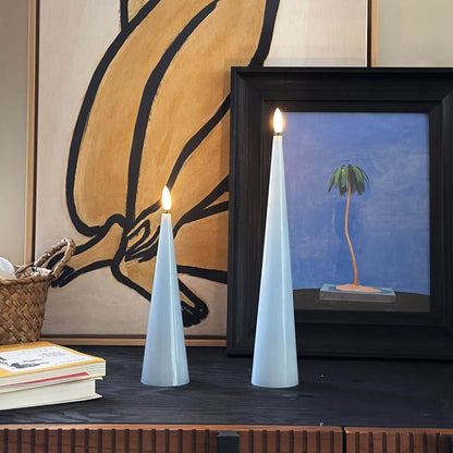 Two light blue cone-shaped candles with a vase of flowers on a wooden surface.