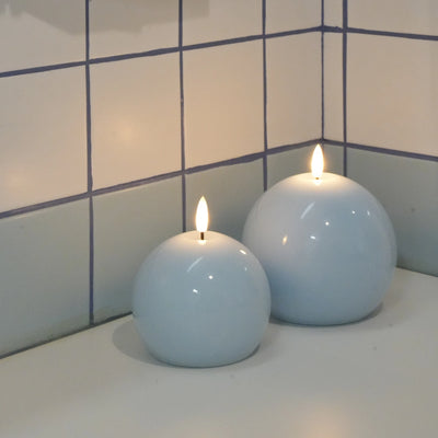 Two spherical candles with flames on a tiled bathroom counter.