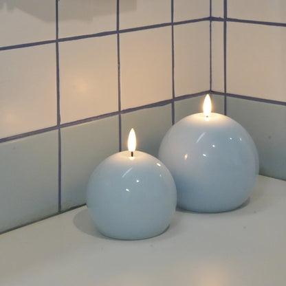 Two spherical candles with flames on a tiled bathroom counter.