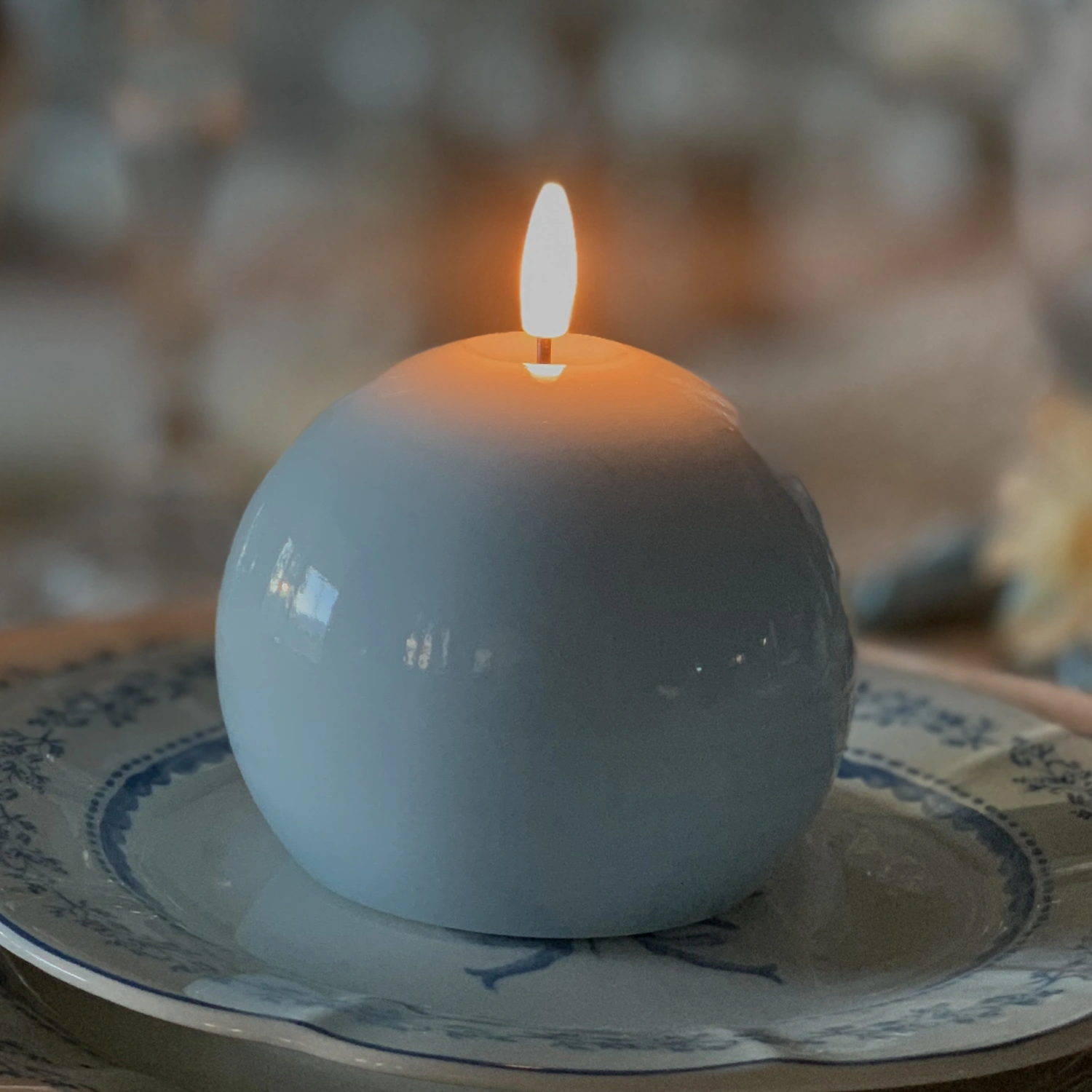 White ceramic candle holder with a lit candle on a decorative plate