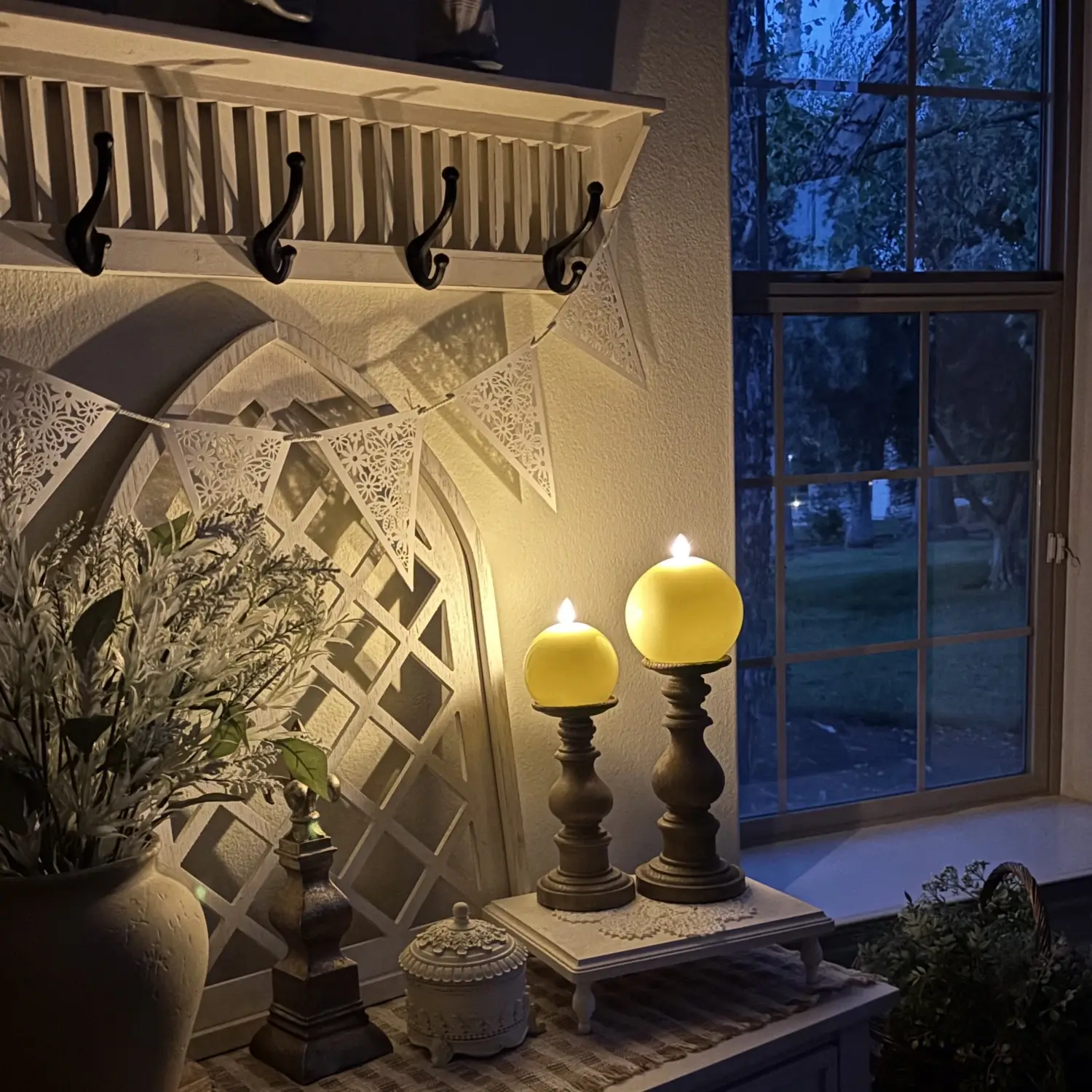 Decorative setup with candles, mirror, and plants in a room with a window view.