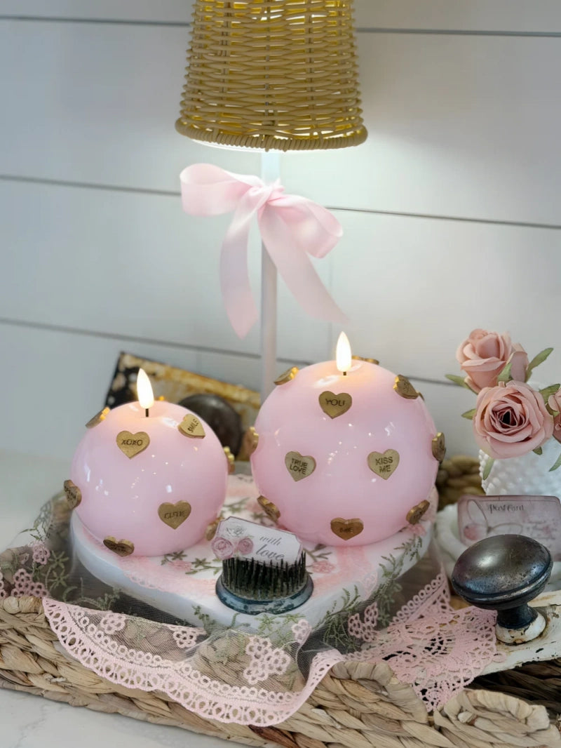 Two pink candles with heart designs on a decorative stand with a white background.