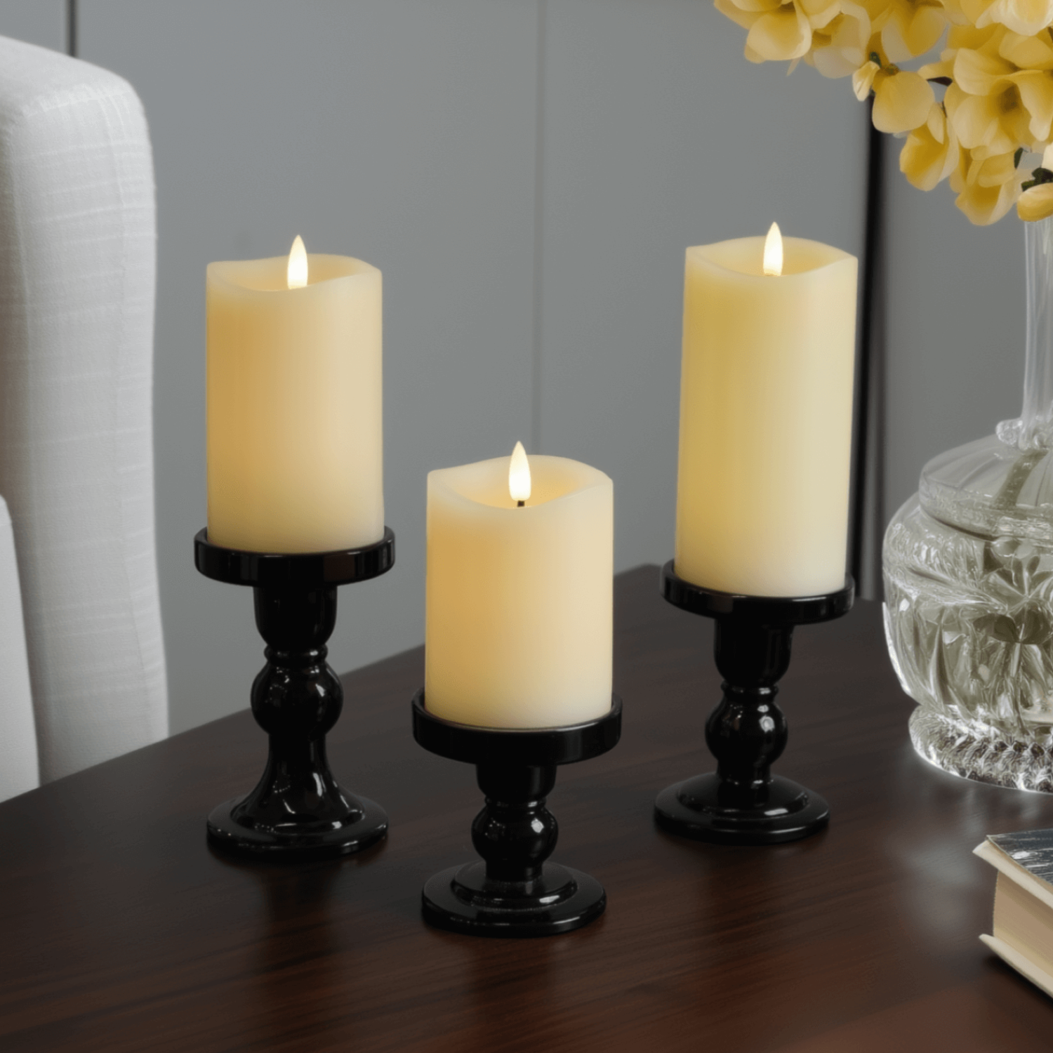 Three lit candles on a wooden surface with a cup and book in the background.