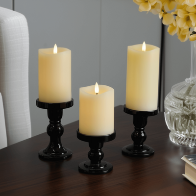 Three lit candles on a wooden surface with a cup and book in the background.