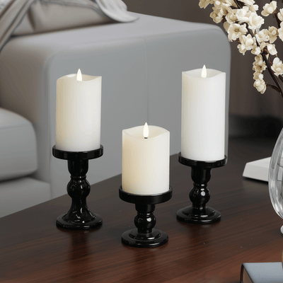 Three lit candles on a table with a book and a cup in a cozy indoor setting.