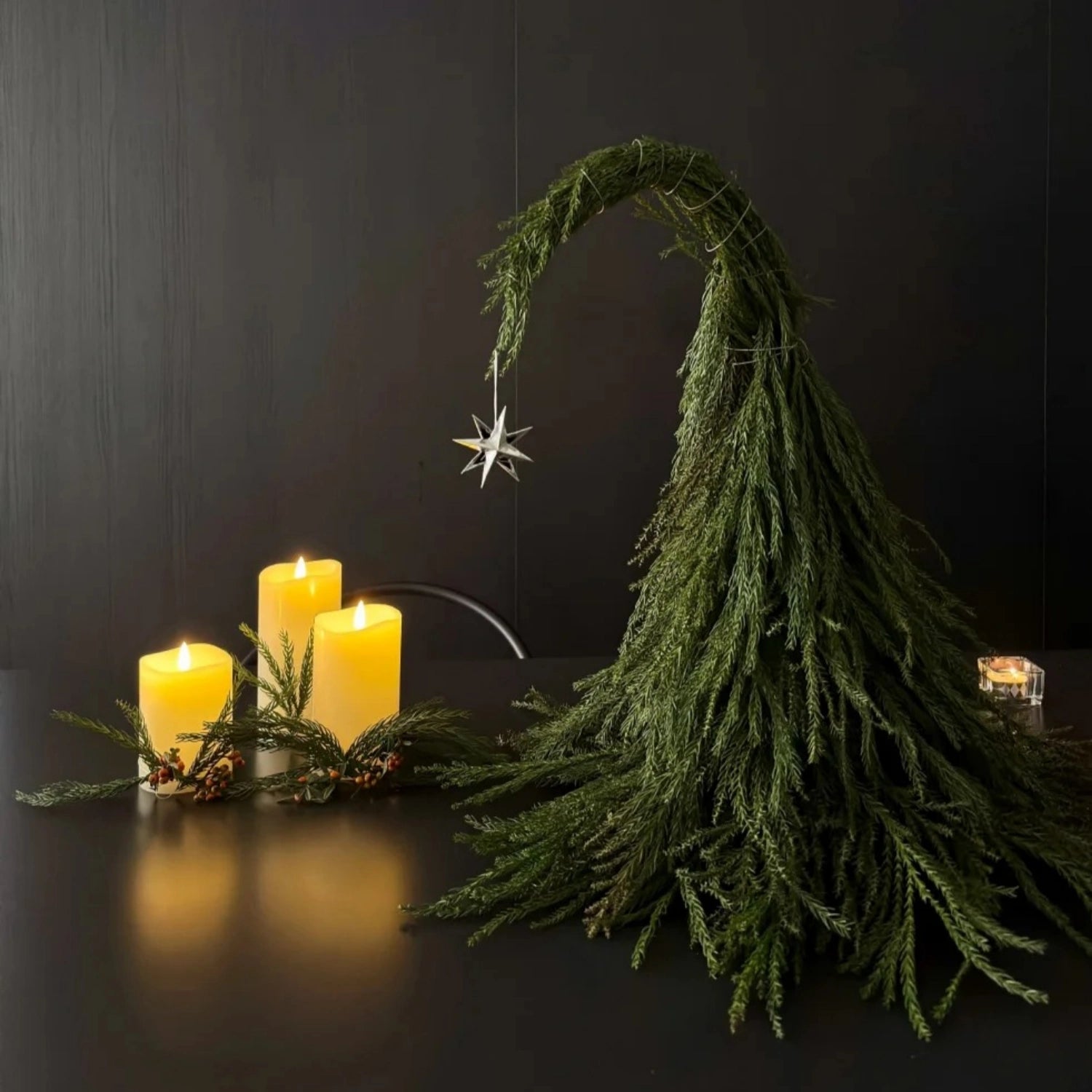 Decorative setup with candles and greenery on a dark surface