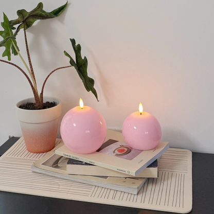 Two pink candles on a stack of books with a plant in the background