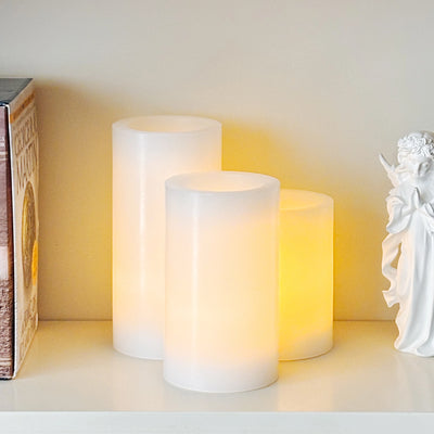 Two white candles on a shelf with a small angel figurine to the right.