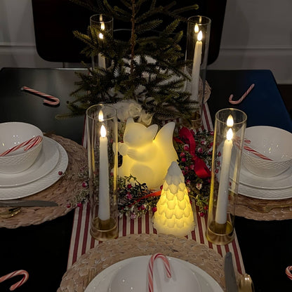 Decorative table setting with candles, a small tree, and candy canes on a striped tablecloth.