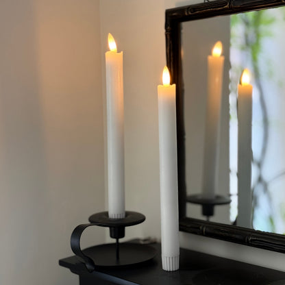 Two lit candles in black holders with a mirror reflecting the scene.