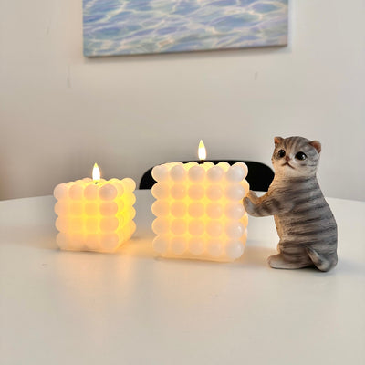 Two bubble-style candles emitting light and a cat figurine on a surface.