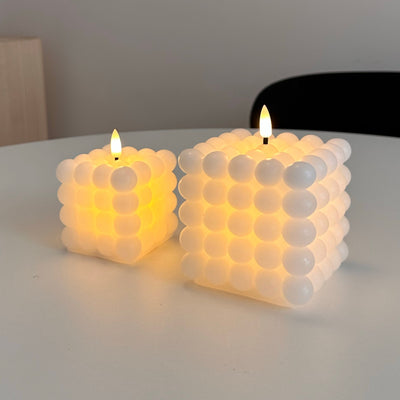 Two bubble-textured candles on a flat surface with a neutral background