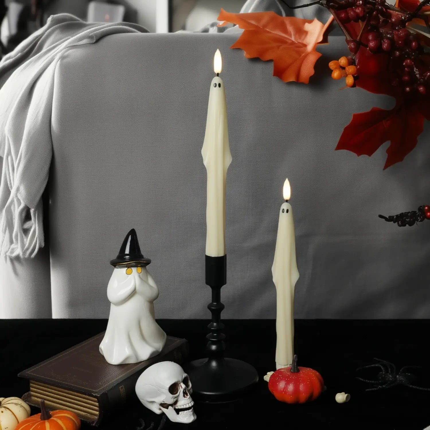 Halloween-themed decor with candles, ghost figurine, and pumpkins on a gray couch.
