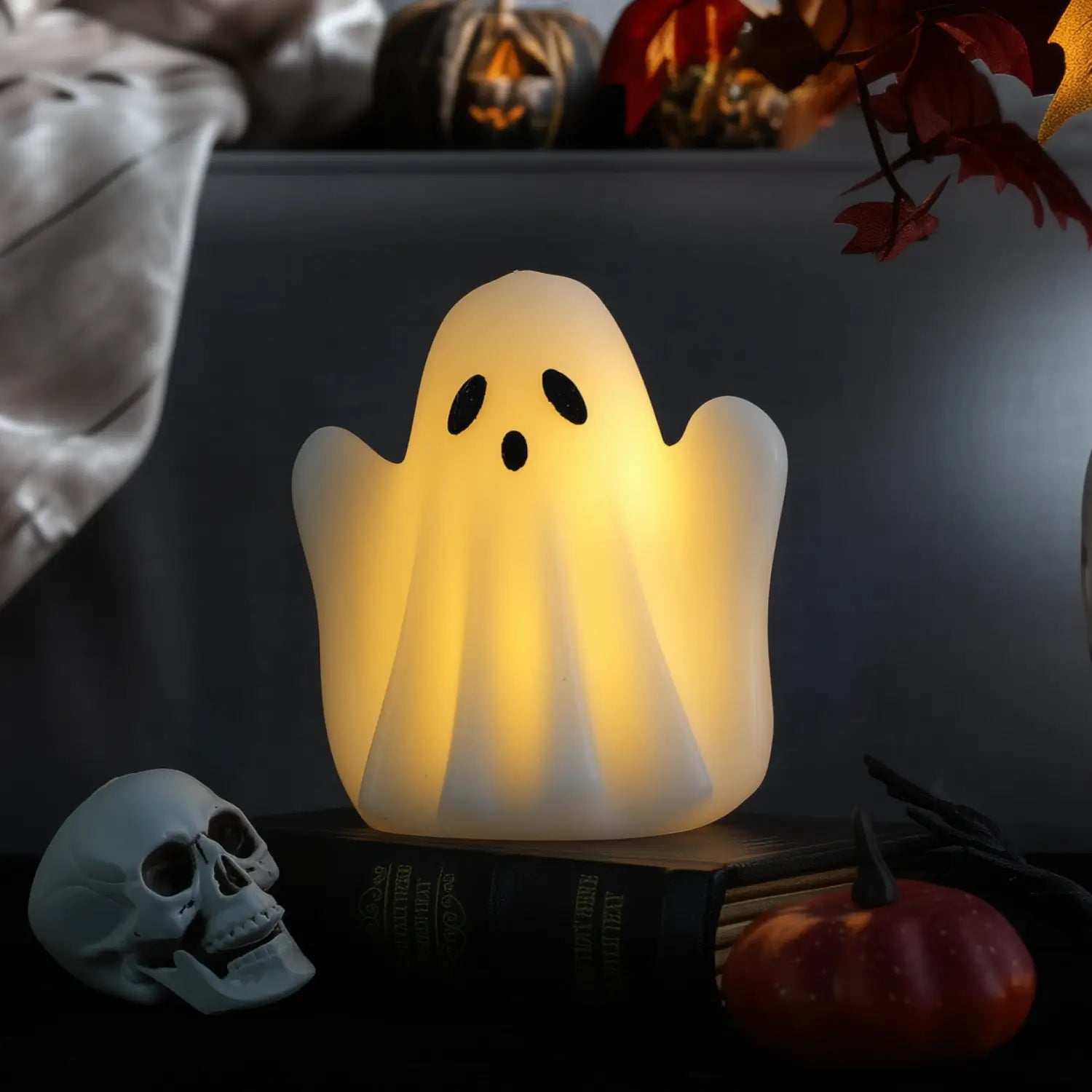 Ghost-shaped lamp on a book with Halloween decorations in the background