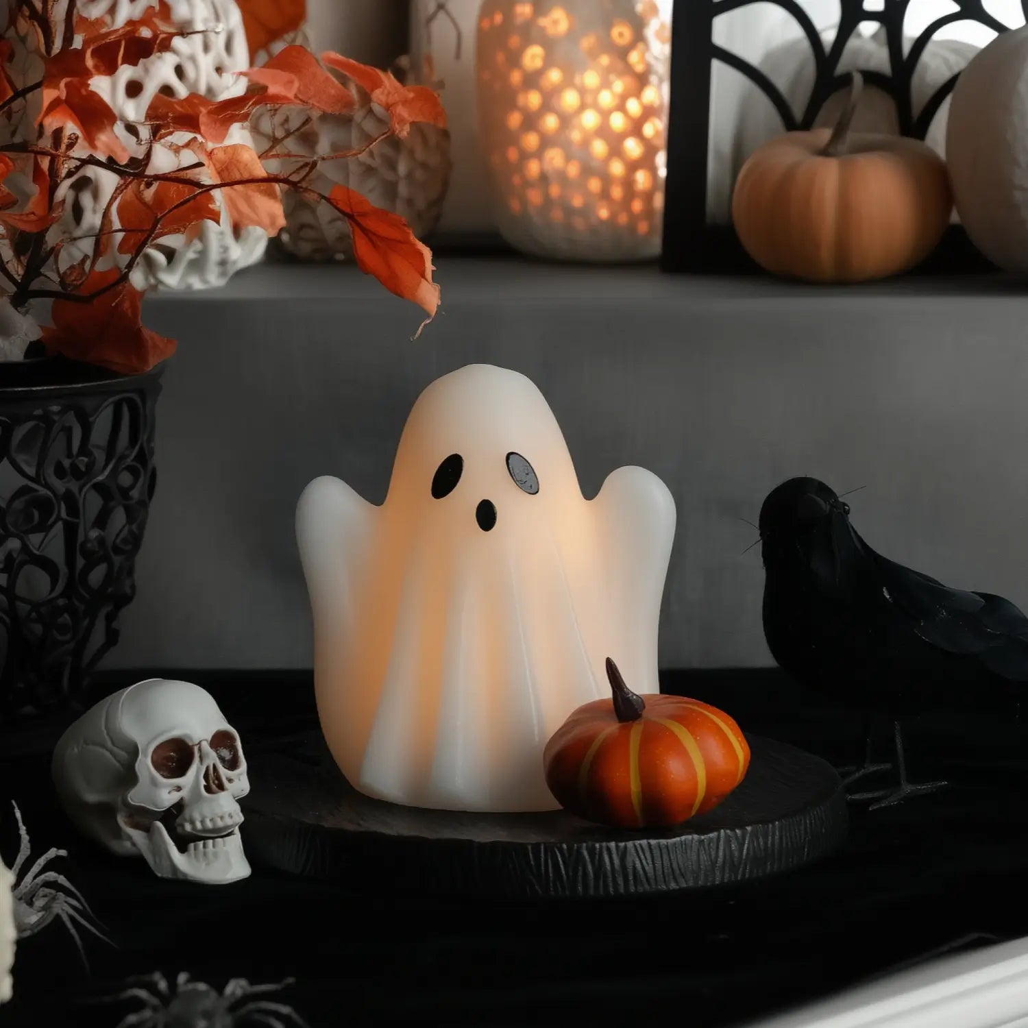 Decorative ghost lamp with Halloween elements like pumpkins and a skull on a dark surface.