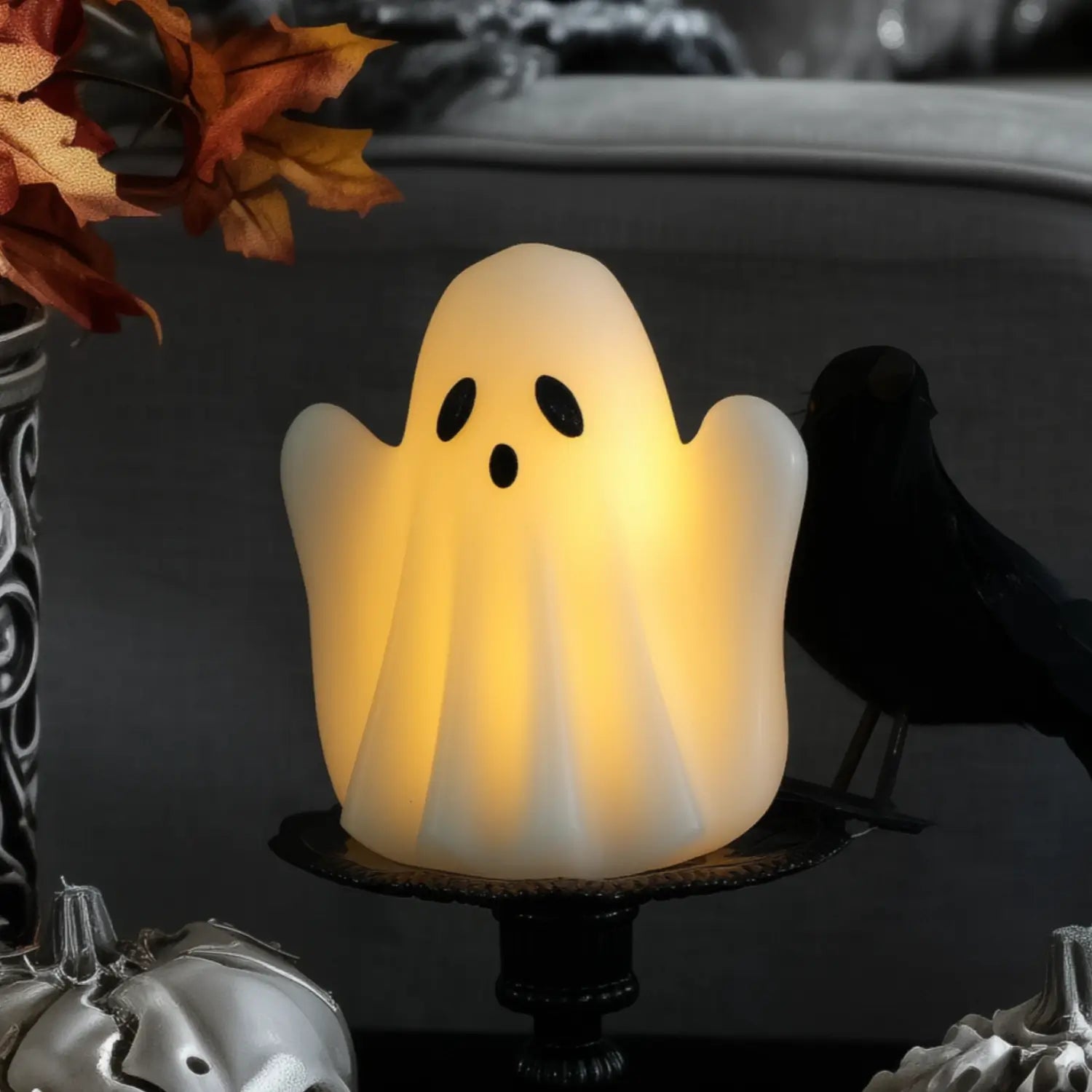 Glowing ghost-shaped candle on a dark background with pumpkins and a crow.