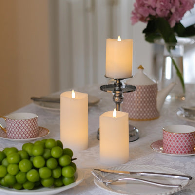 Decorative table setting with candles and greenery on a white tablecloth.