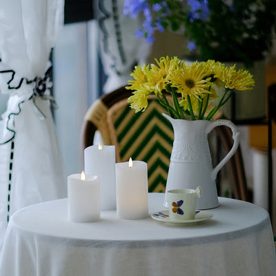 White table with candles, a vase of yellow flowers, and a teacup on a blurred background