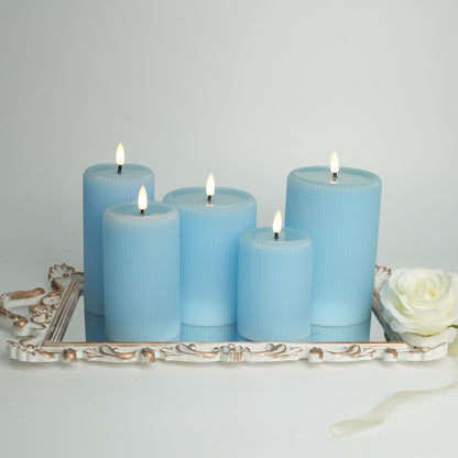 Set of five blue candles on a decorative tray with a white flower and ribbon against a light gray background